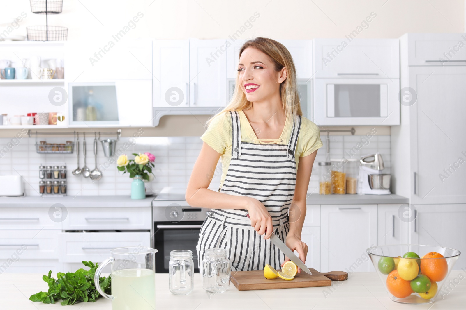 Photo of Young woman preparing lemonade on table in kitchen. Natural detox drink