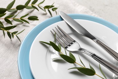 Photo of Stylish setting with cutlery and eucalyptus leaves on light grey table, closeup