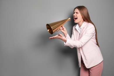 Young woman shouting into megaphone on grey background
