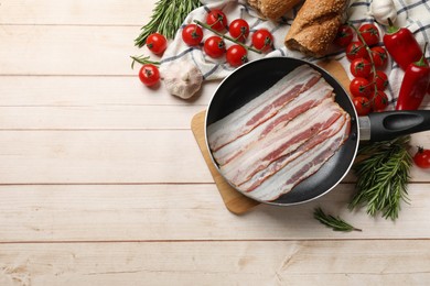 Slices of raw bacon in frying pan and fresh products on wooden table, flat lay. Space for text