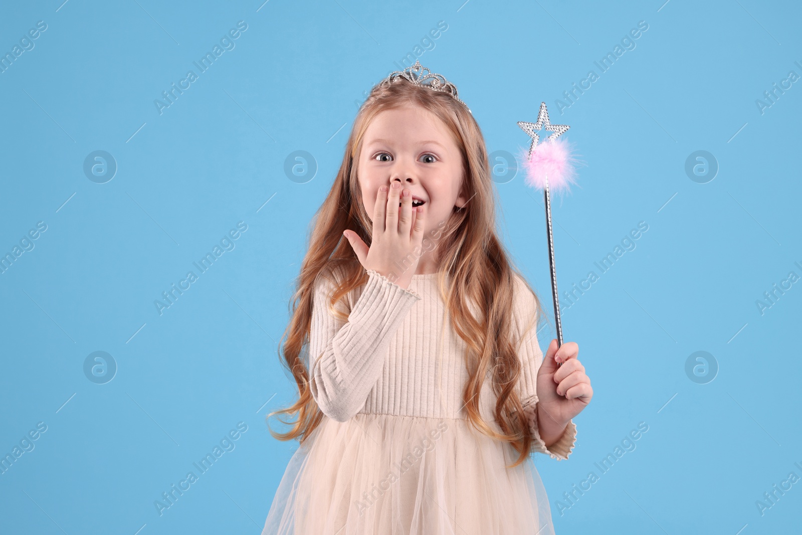 Photo of Cute girl in diadem with magic wand on light blue background. Little princess