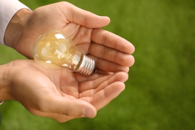 Photo of Man holding lamp bulb against green background. Space for text
