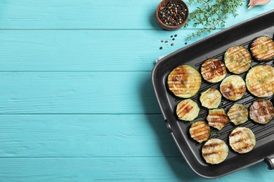 Photo of Frying pan with grilled zucchini slices on blue wooden table, flat lay. Space for text