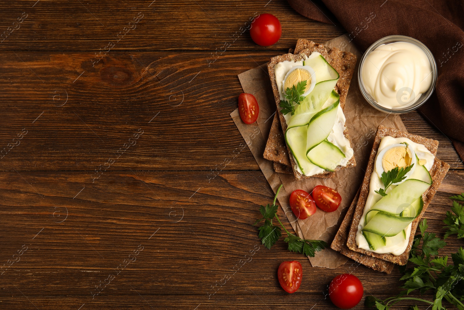 Photo of Fresh rye crispbreads with quail egg, cream cheese and cucumber slices on wooden table, flat lay. Space for text