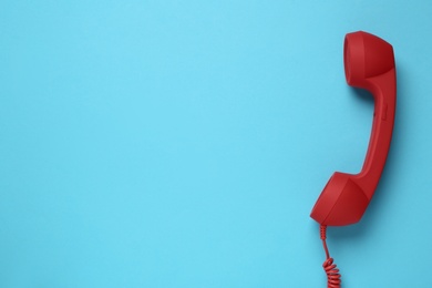 Photo of Red corded telephone handset on light blue background, top view. Hotline concept