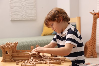 Photo of Cute little boy playing with wooden construction set at table in room. Child's toy