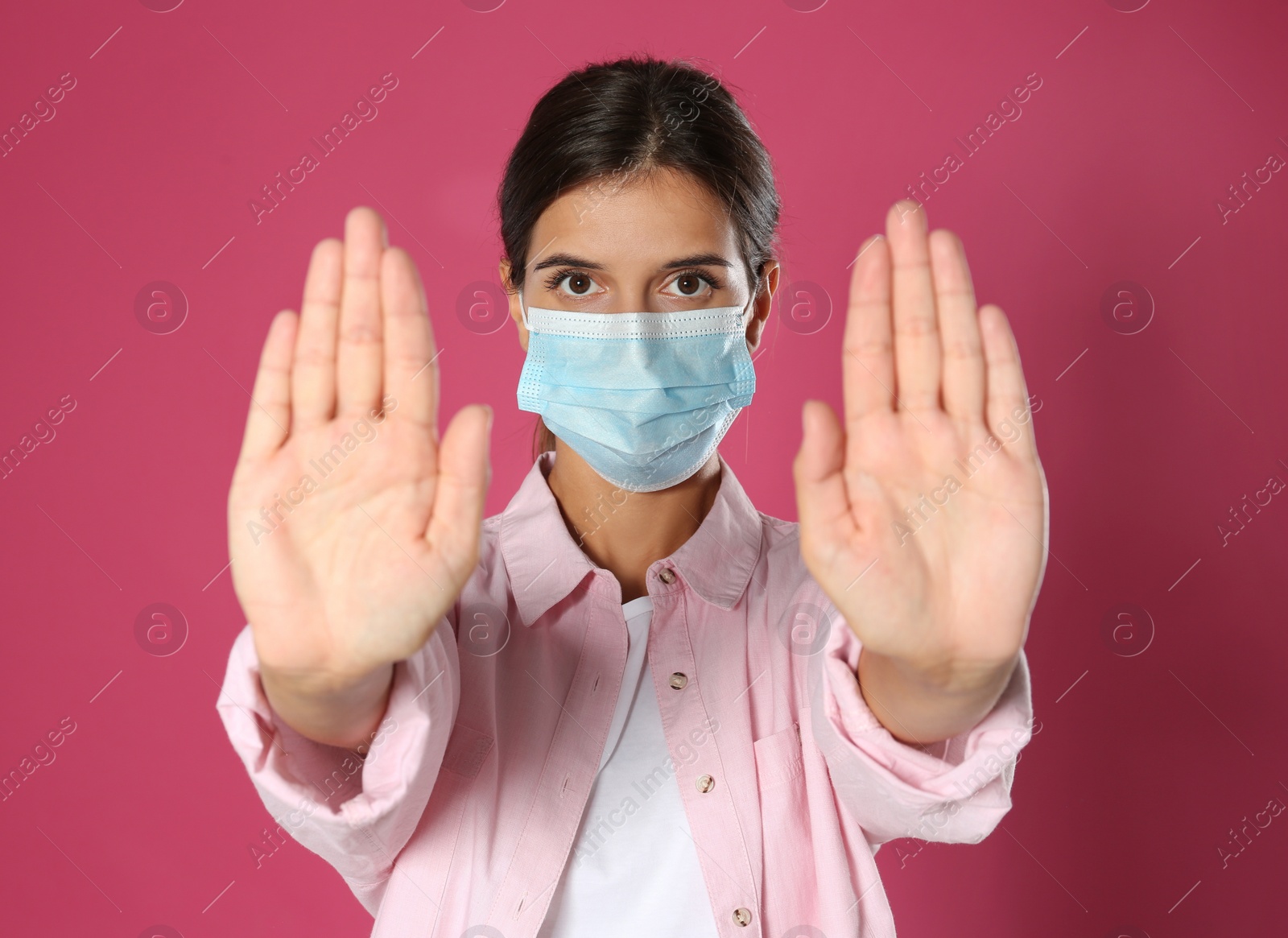 Photo of Woman in protective mask showing stop gesture on pink background. Prevent spreading of coronavirus