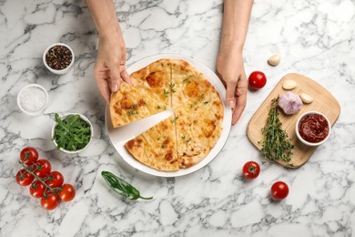 Photo of Top view of woman taking delicious khachapuri piece with cheese and thyme at white marble table