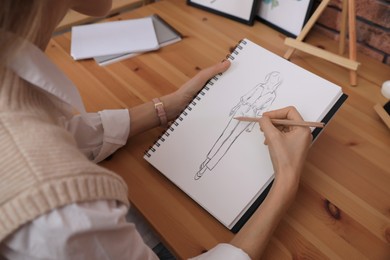 Image of Fashion designer creating new look. Woman drawing sketch in book with pencil at wooden table, closeup