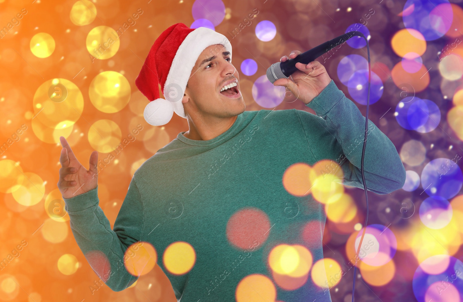 Image of Happy man in Santa hat singing on bright background, bokeh effect