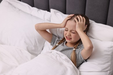 Photo of Little girl suffering from headache in bed