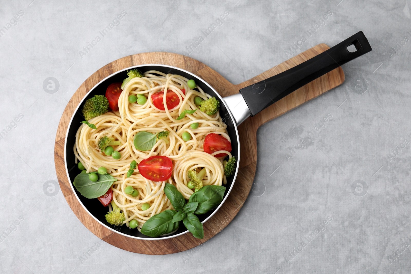 Photo of Delicious pasta primavera in frying pan and ingredients on light gray table, top view