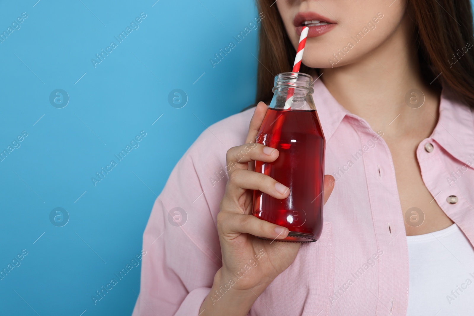 Photo of Young woman drinking juice from glass bottle on light blue background, closeup. Space for text