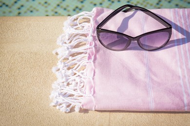 Stylish sunglasses and blanket near outdoor pool on sunny day, space for text