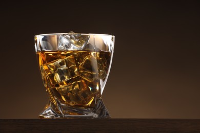 Photo of Whiskey with ice cubes in glass on table against brown background. Space for text