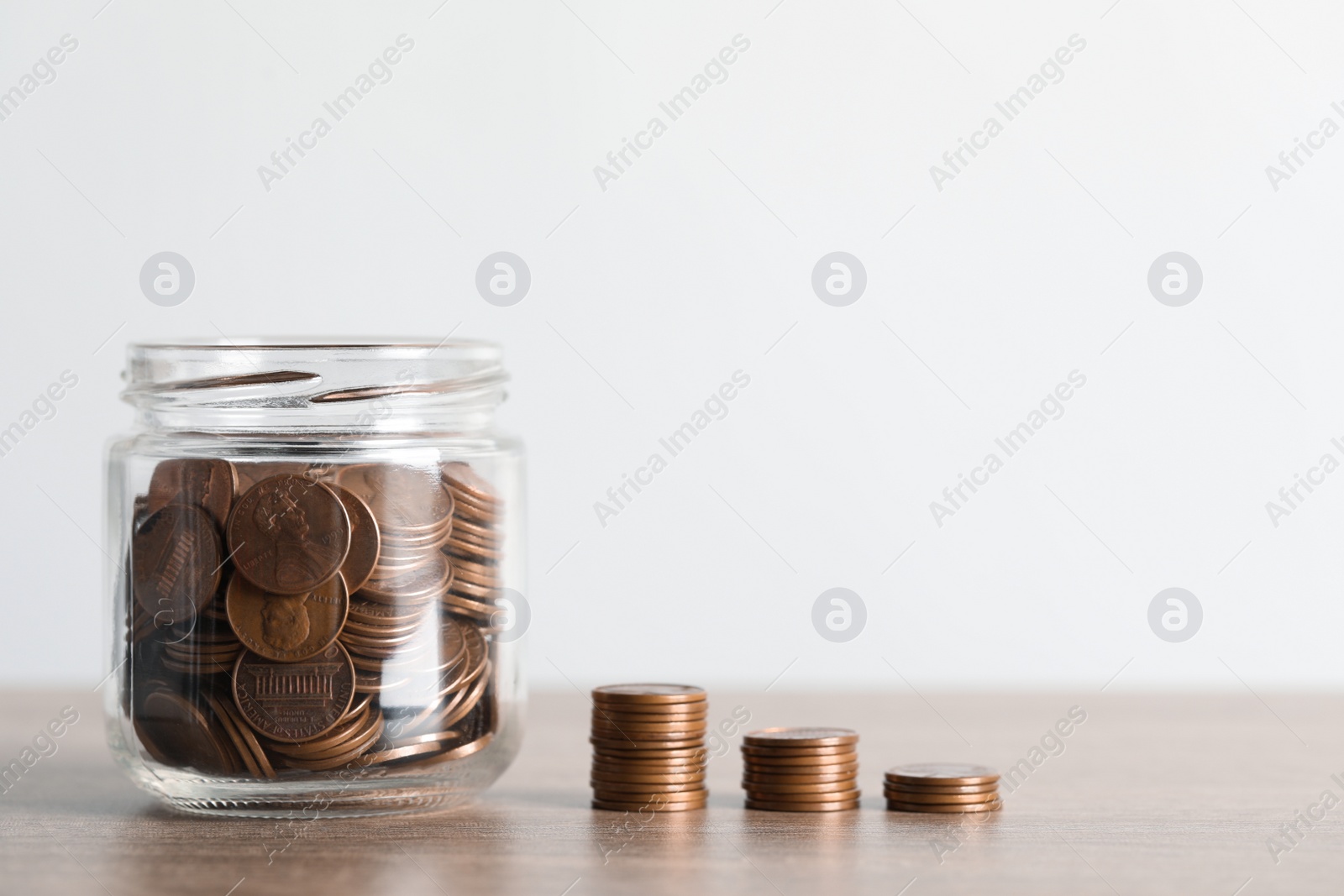 Photo of Glass jar with money and stack of coins on wooden table