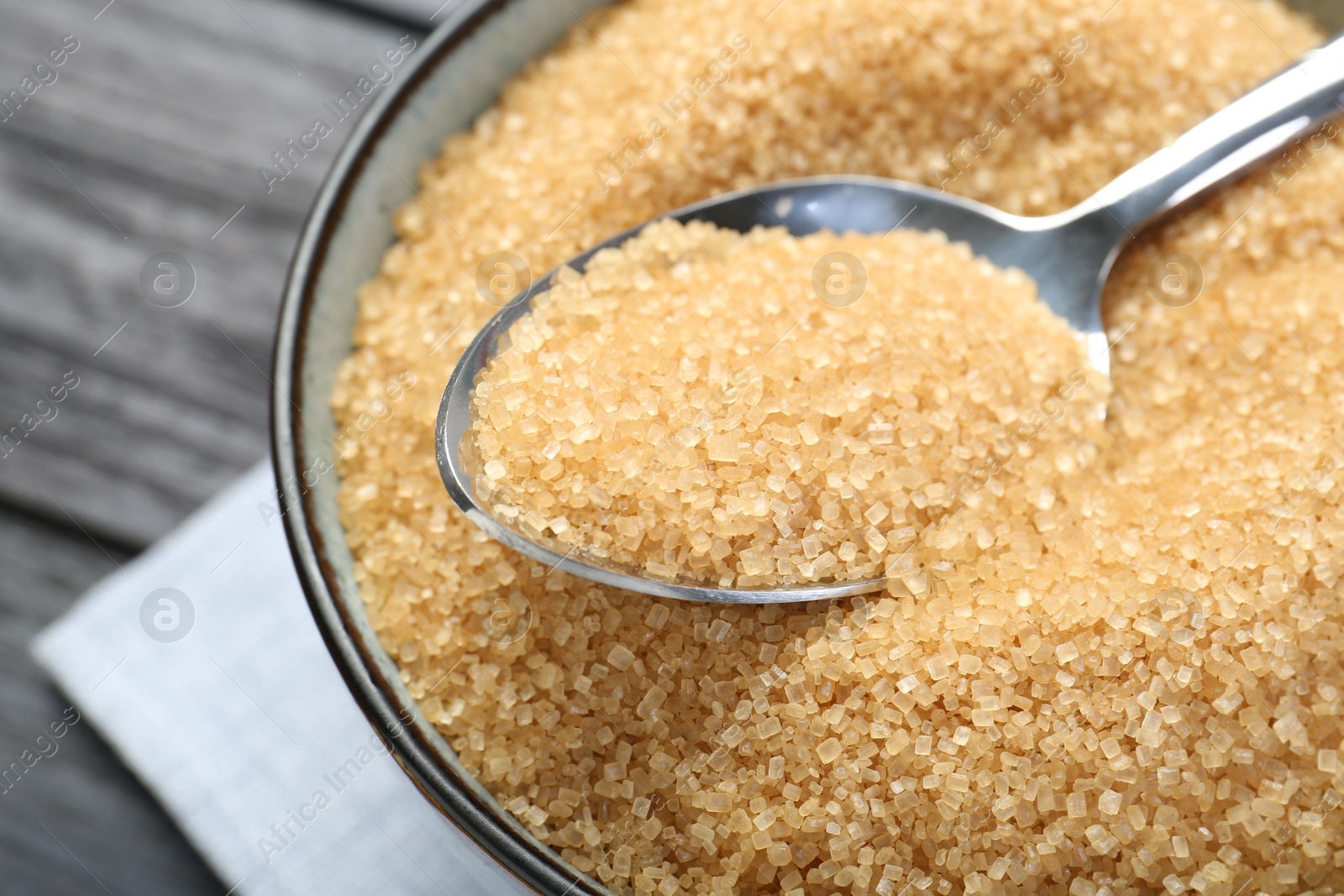 Photo of Brown sugar in bowl and spoon on black table, closeup