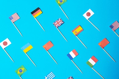 Photo of Many small paper flags of different countries on light blue background, flat lay