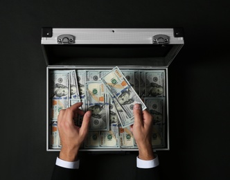 Photo of Businessman counting money over suitcase on dark background, top view