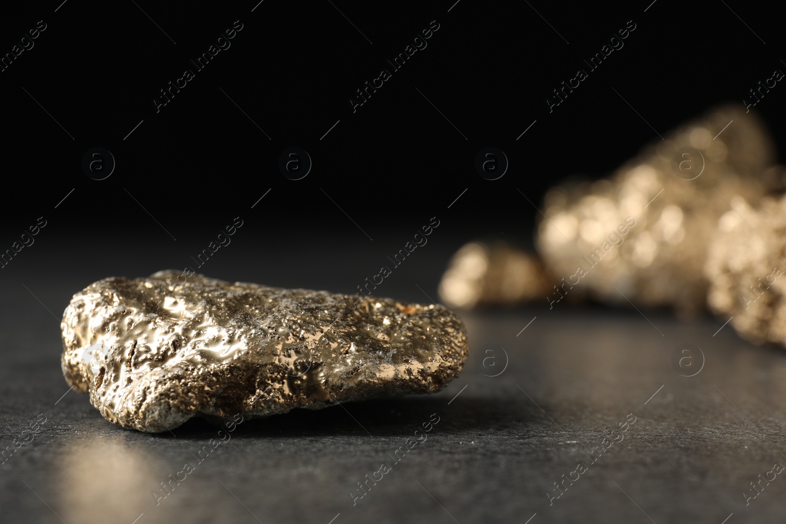 Photo of Shiny gold nugget on grey surface, closeup. Space for text