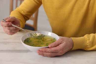 Man eating delicious chicken soup at light marble table indoors, closeup