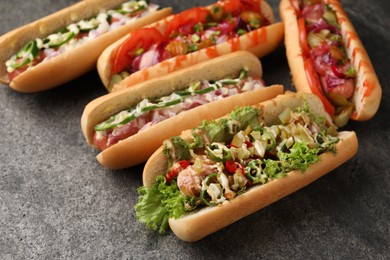 Photo of Delicious hot dogs with different toppings on grey table, closeup