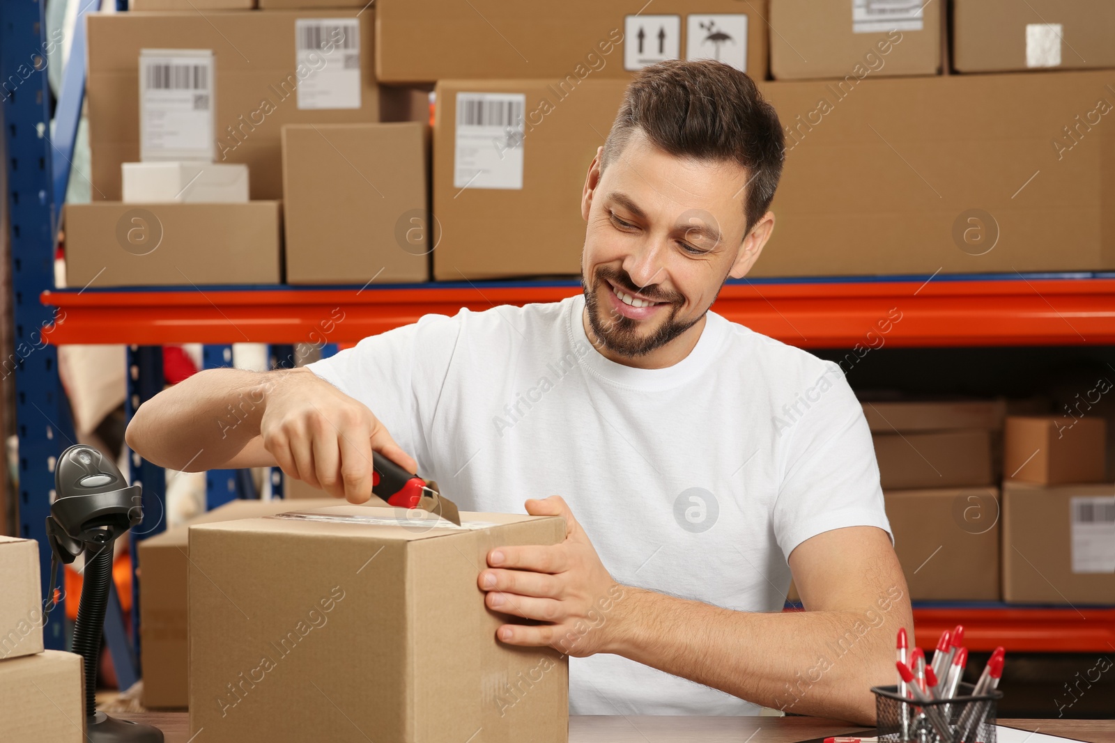 Photo of Post office worker with utility knife opening parcel indoors