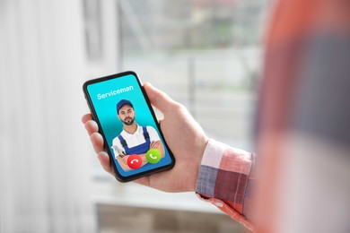 Man with smartphone calling professional serviceman indoors, closeup