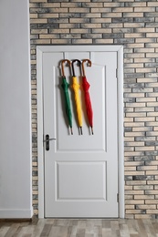 Colorful umbrellas hanging on door in brick wall