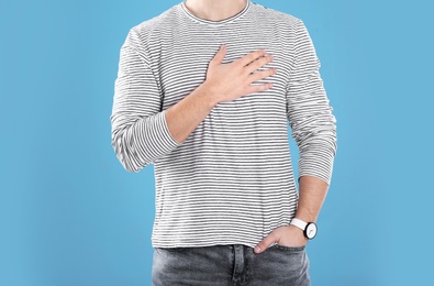 Young man holding hand near heart on color background, closeup