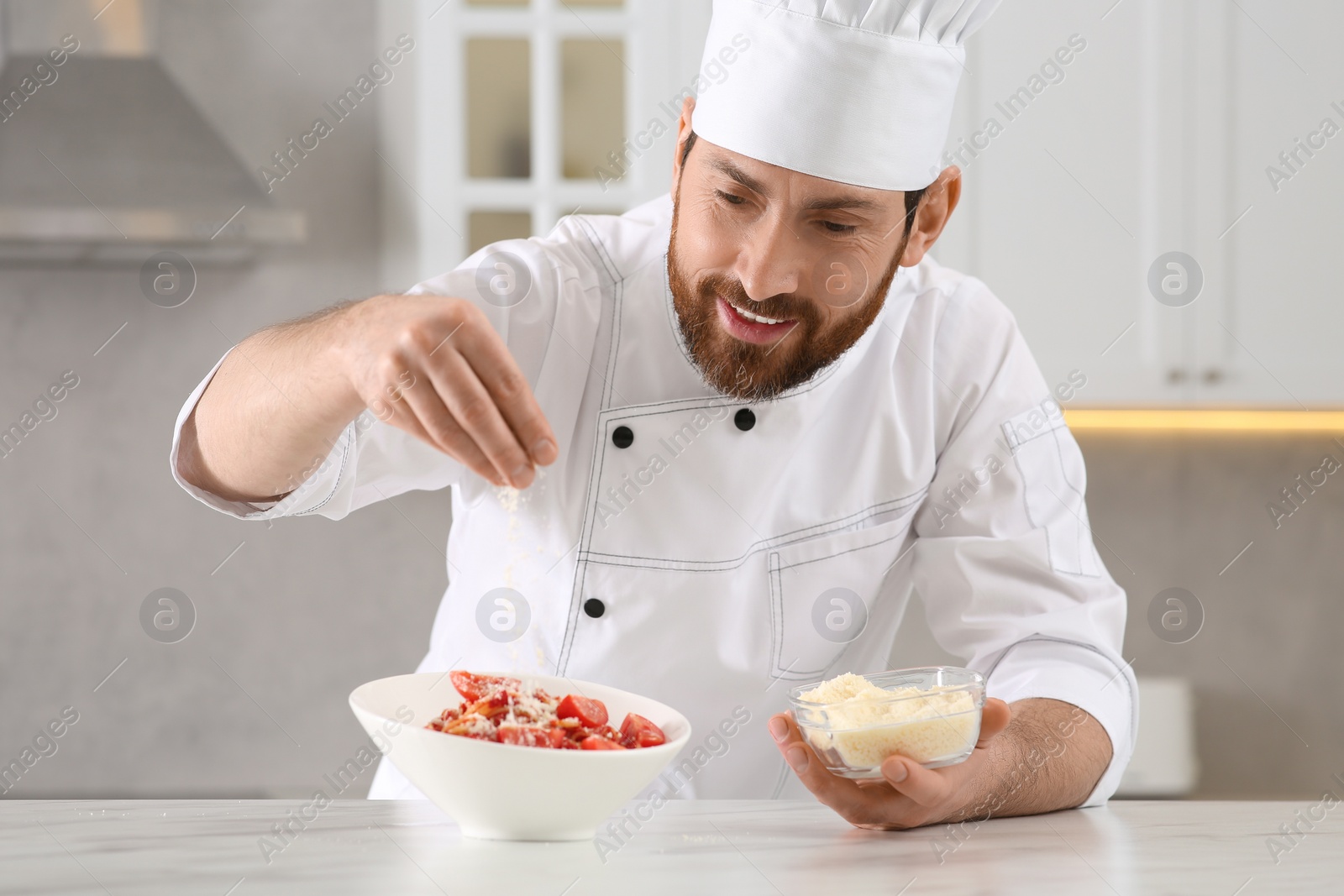 Photo of Professional chef adding grated cheese into delicious spaghetti at marble table