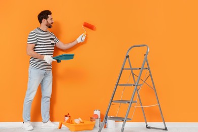 Photo of Designer painting orange wall with roller indoors