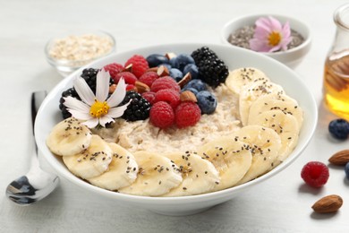 Photo of Tasty oatmeal porridge with berries, banana and chia seeds served on light wooden table, closeup