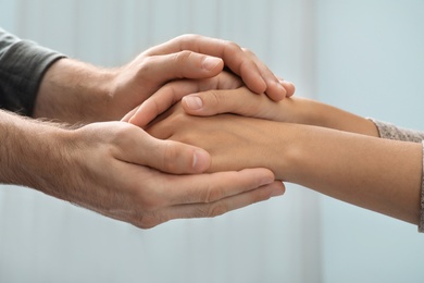 Photo of Man holding woman's hands against blurred background, closeup. Concept of support and help