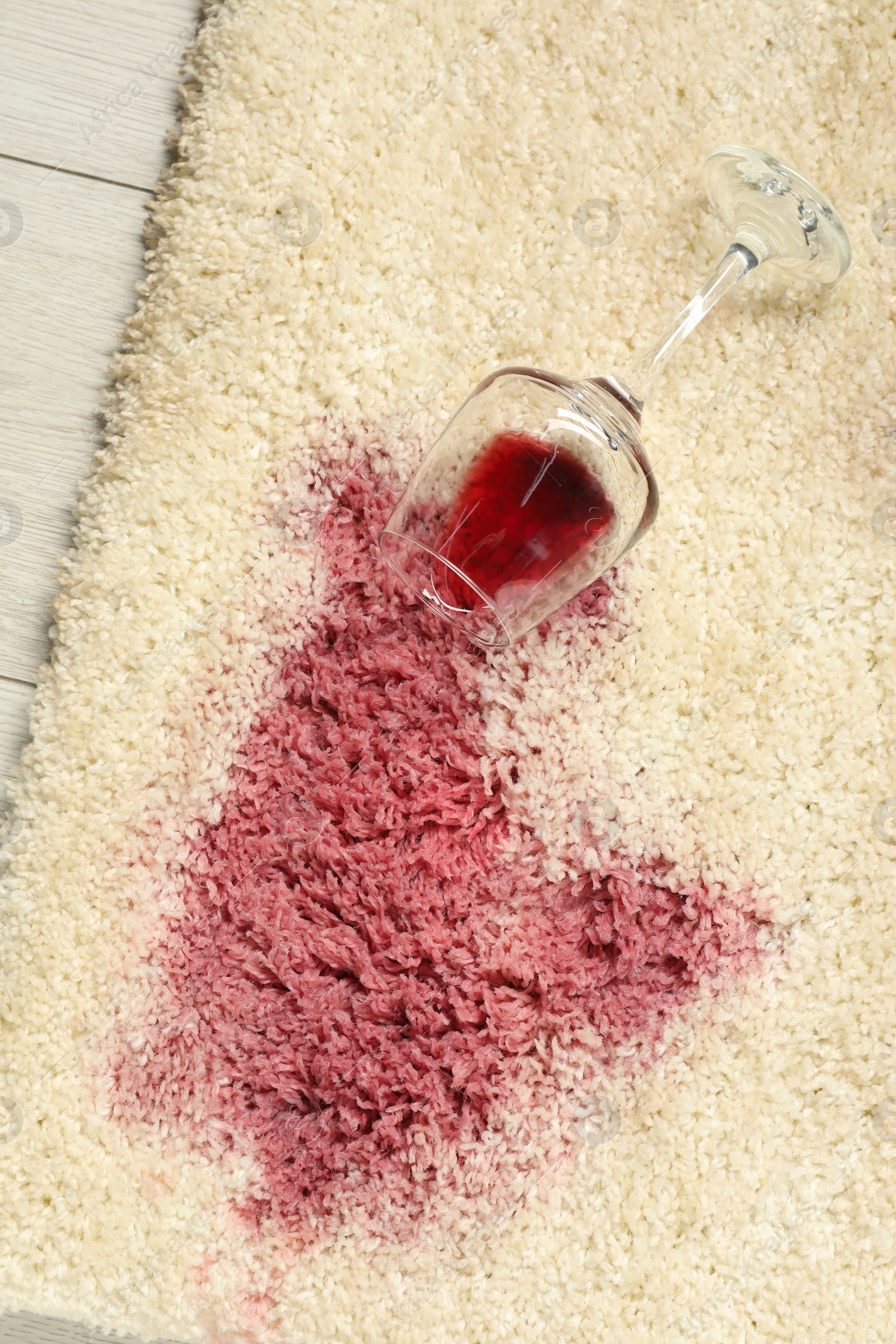 Photo of Overturned glass and spilled red wine on beige carpet, top view
