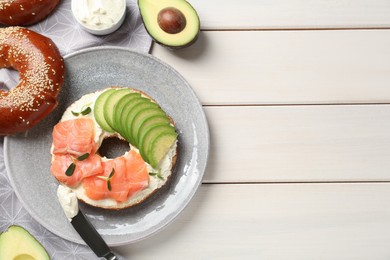 Delicious bagel with cream cheese, salmon and avocado on white wooden table, flat lay. Space for text