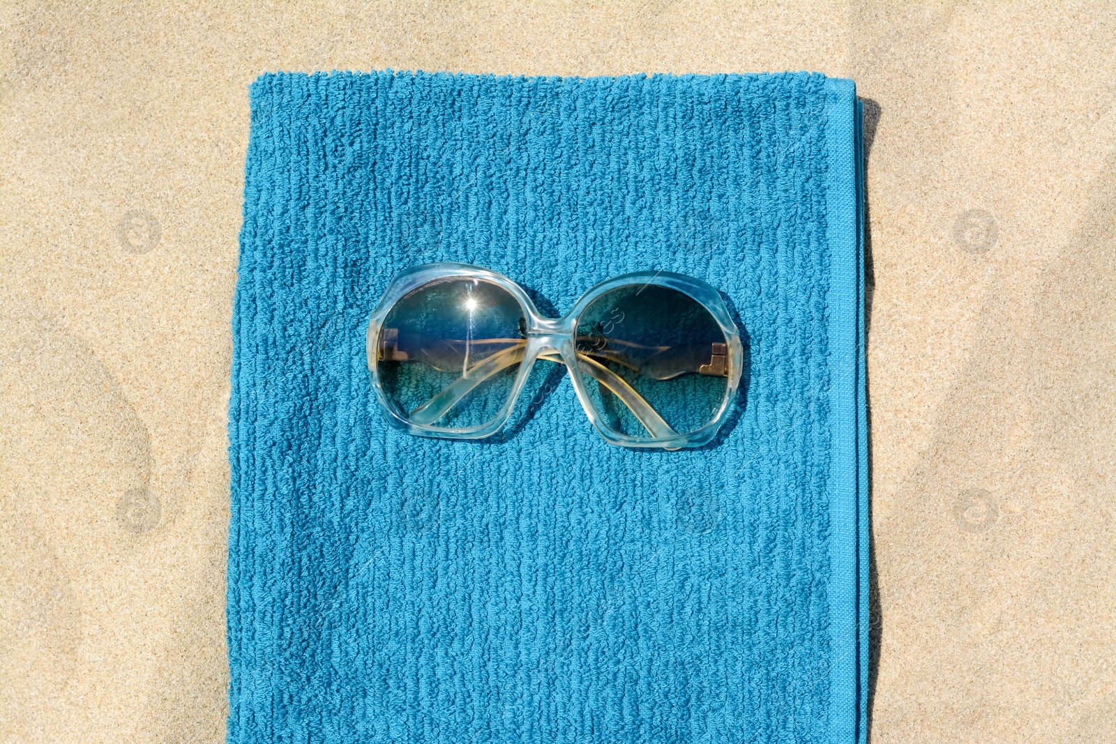 Photo of Soft blue beach towel with sunglasses on sand, top view