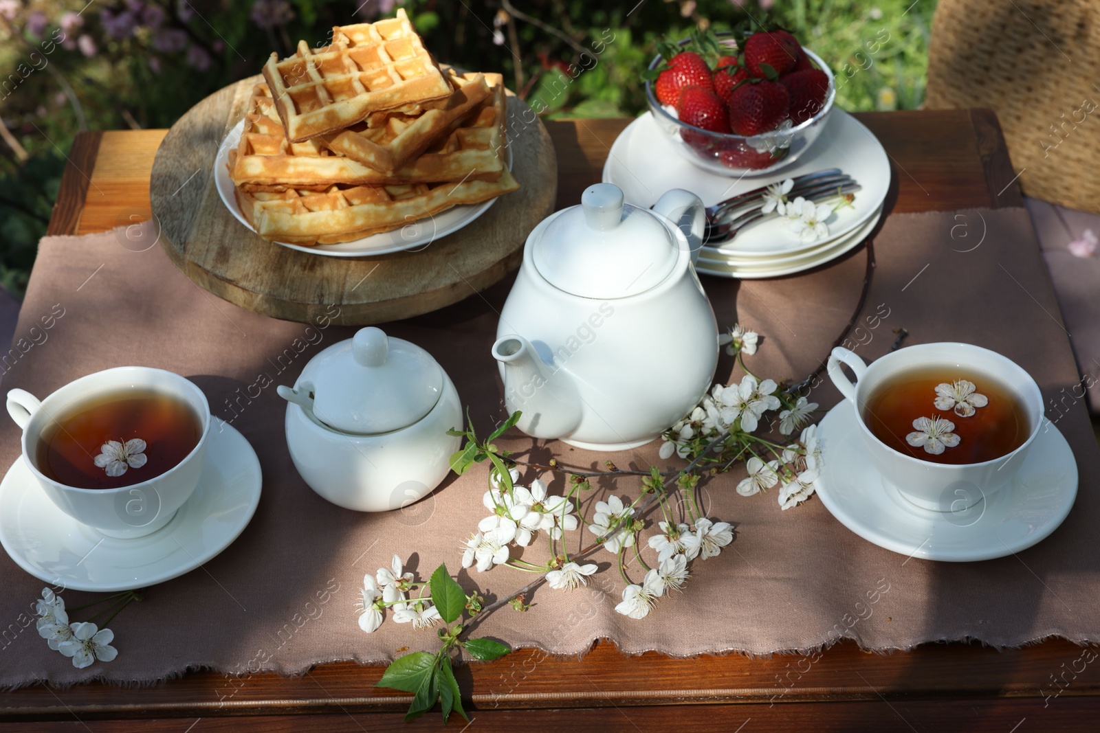 Photo of Beautiful spring flowers, freshly baked waffles and ripe strawberries on table served for tea drinking in garden