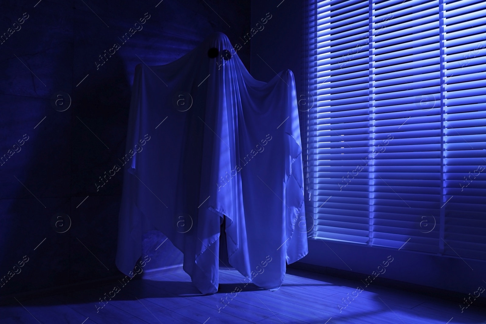 Photo of Creepy ghost. Woman covered with sheet near window in blue light