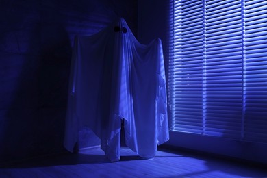 Creepy ghost. Woman covered with sheet near window in blue light