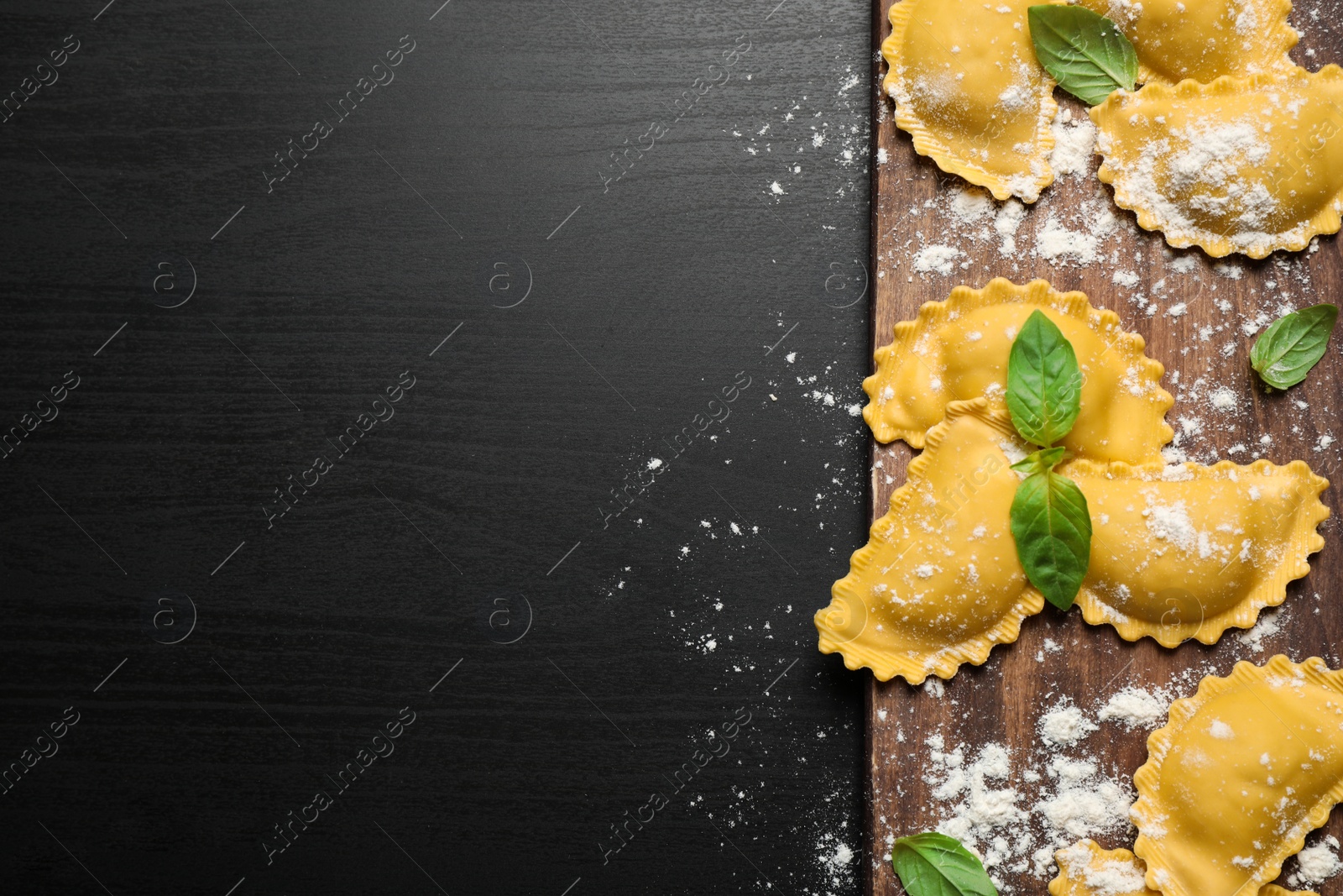 Photo of Raw ravioli with basil on black wooden table, flat lay and space for text. Italian pasta