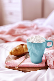 Photo of Morning coffee with marshmallow and croissant on bed indoors. Space for text