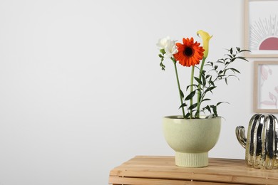 Photo of Stylish ikebana as house decor. Beautiful fresh flowers on wooden table near white wall, space for text