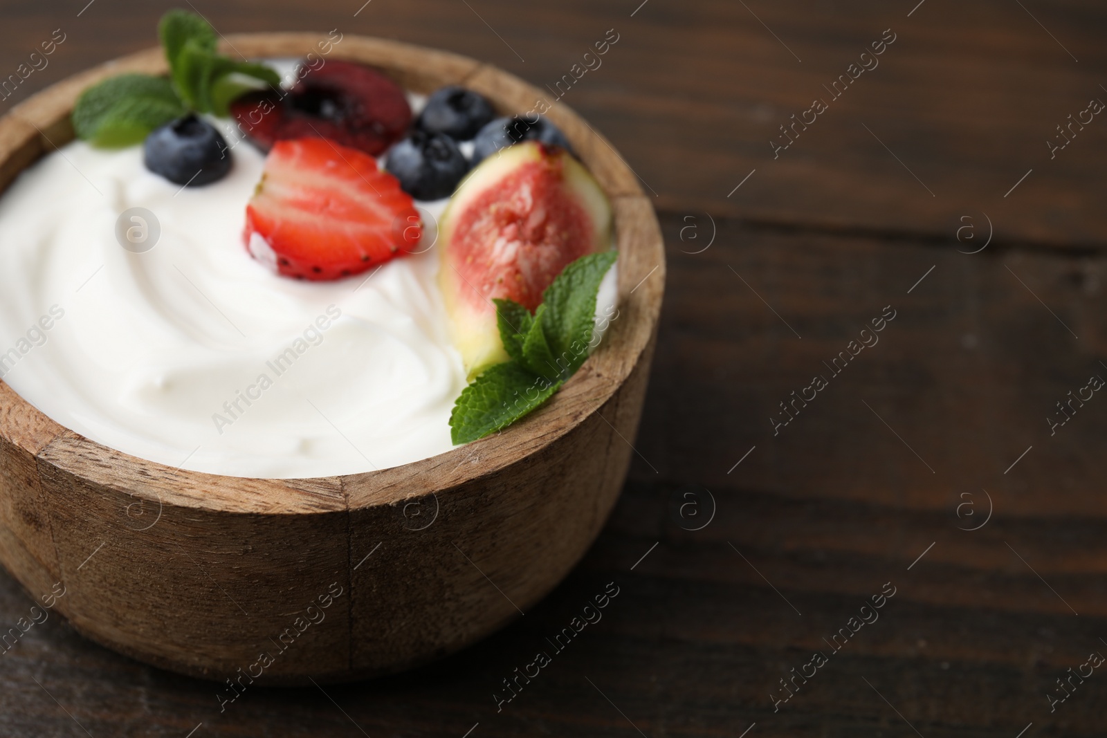 Photo of Bowl with yogurt, berries, fruits and mint on wooden table, closeup. Space for text