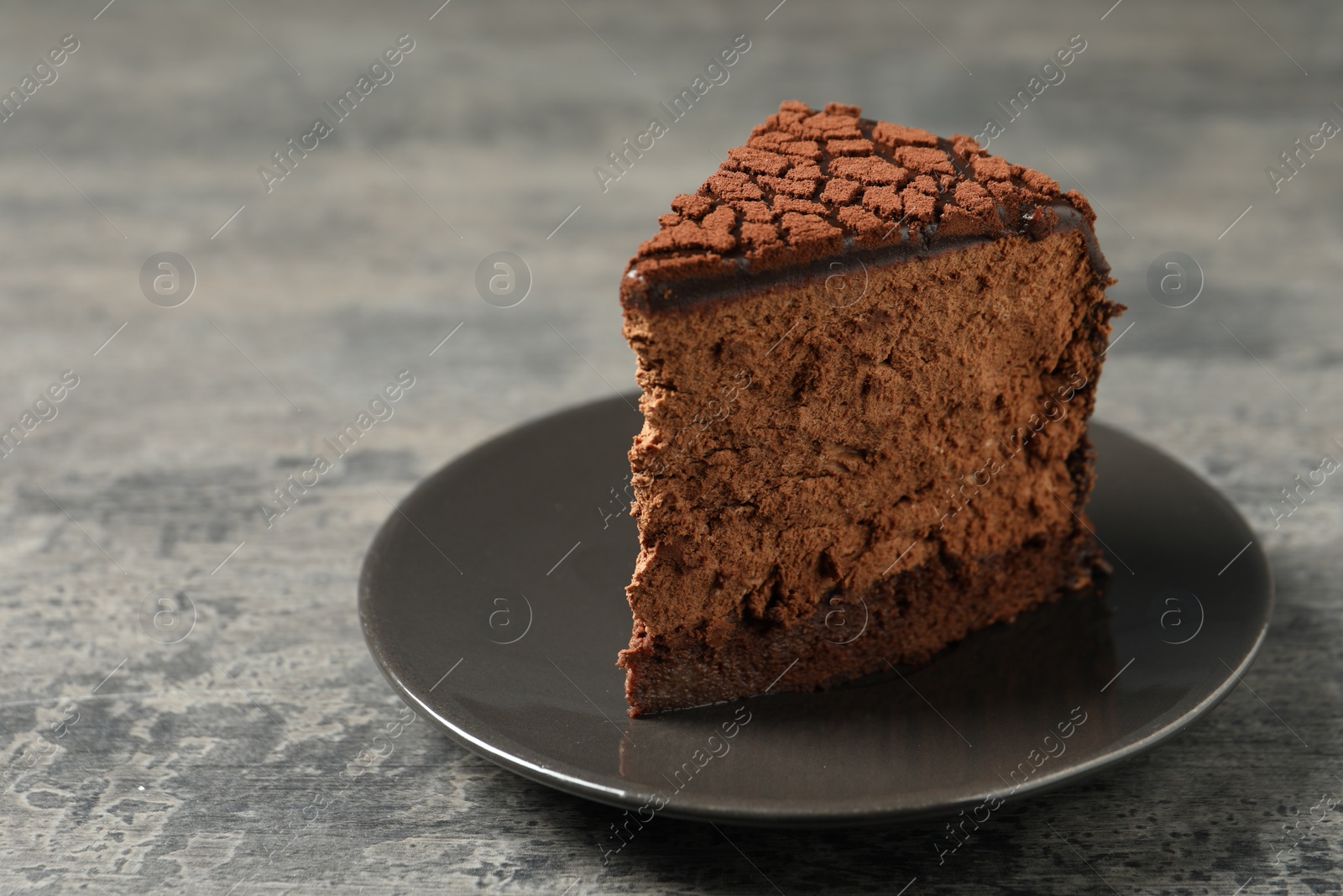 Photo of Piece of delicious chocolate truffle cake on grey textured table, closeup
