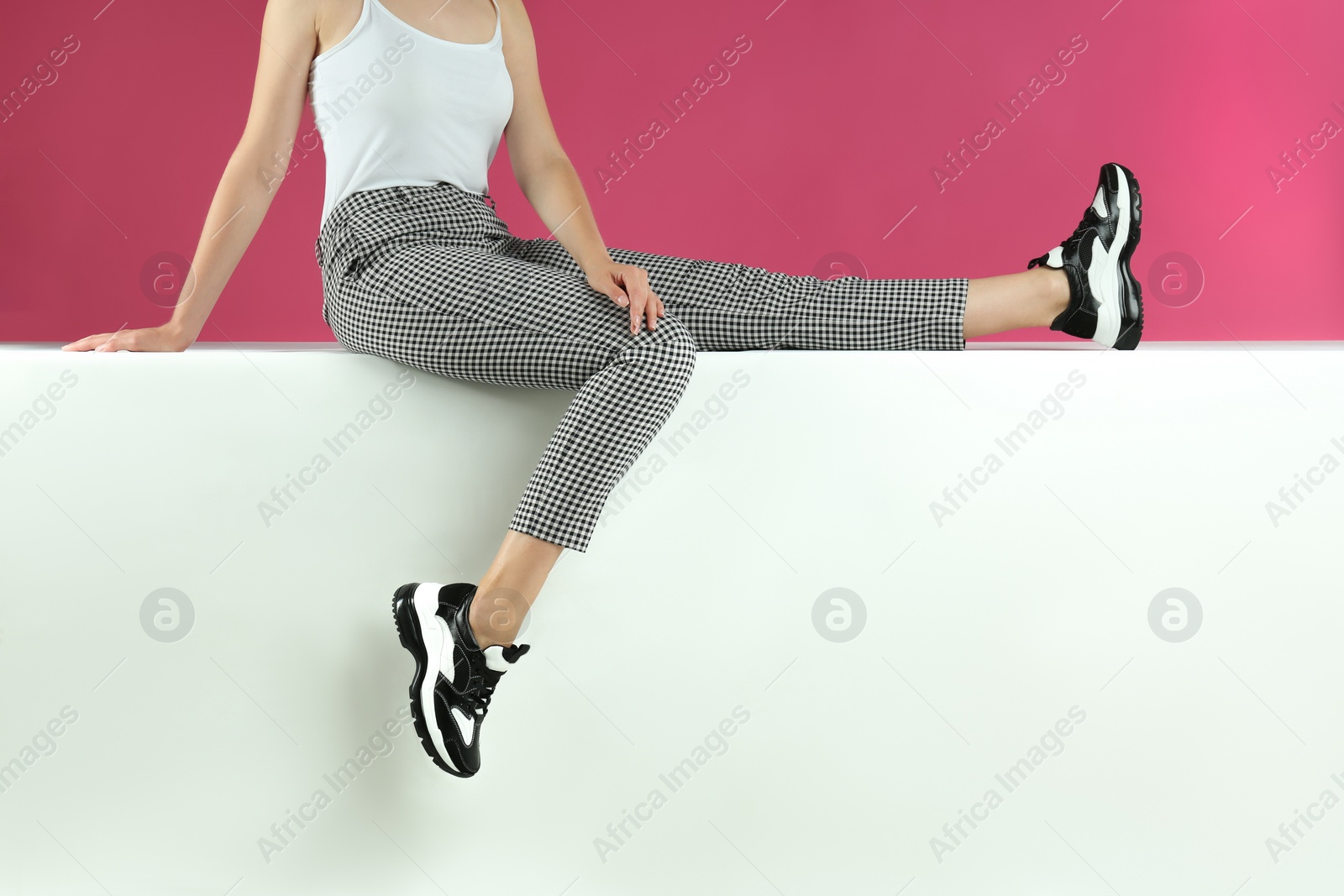 Photo of Woman in stylish sneakers sitting on color background, closeup