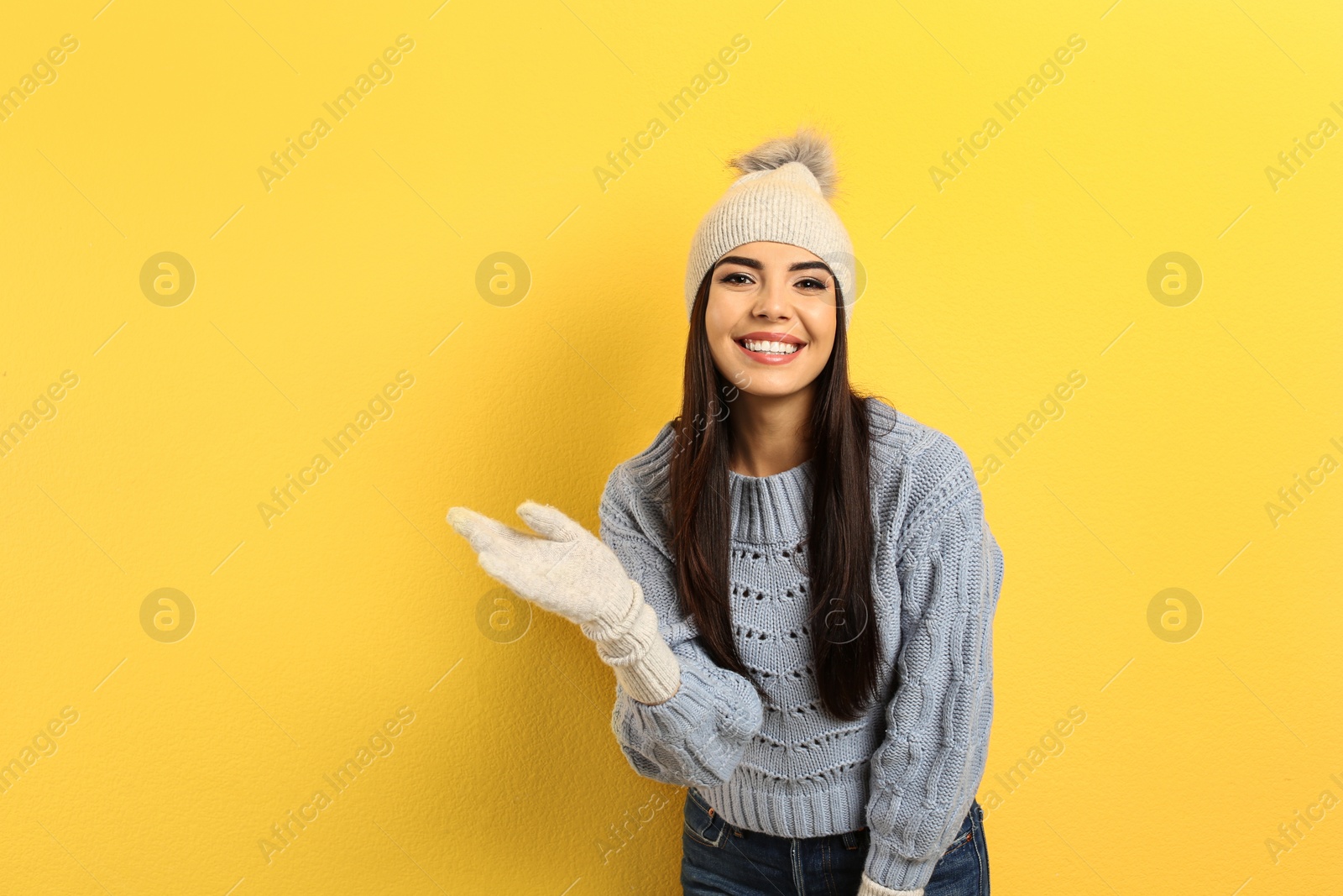 Photo of Happy young woman in warm clothes on yellow background. Winter vacation