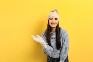 Photo of Happy young woman in warm clothes on yellow background. Winter vacation