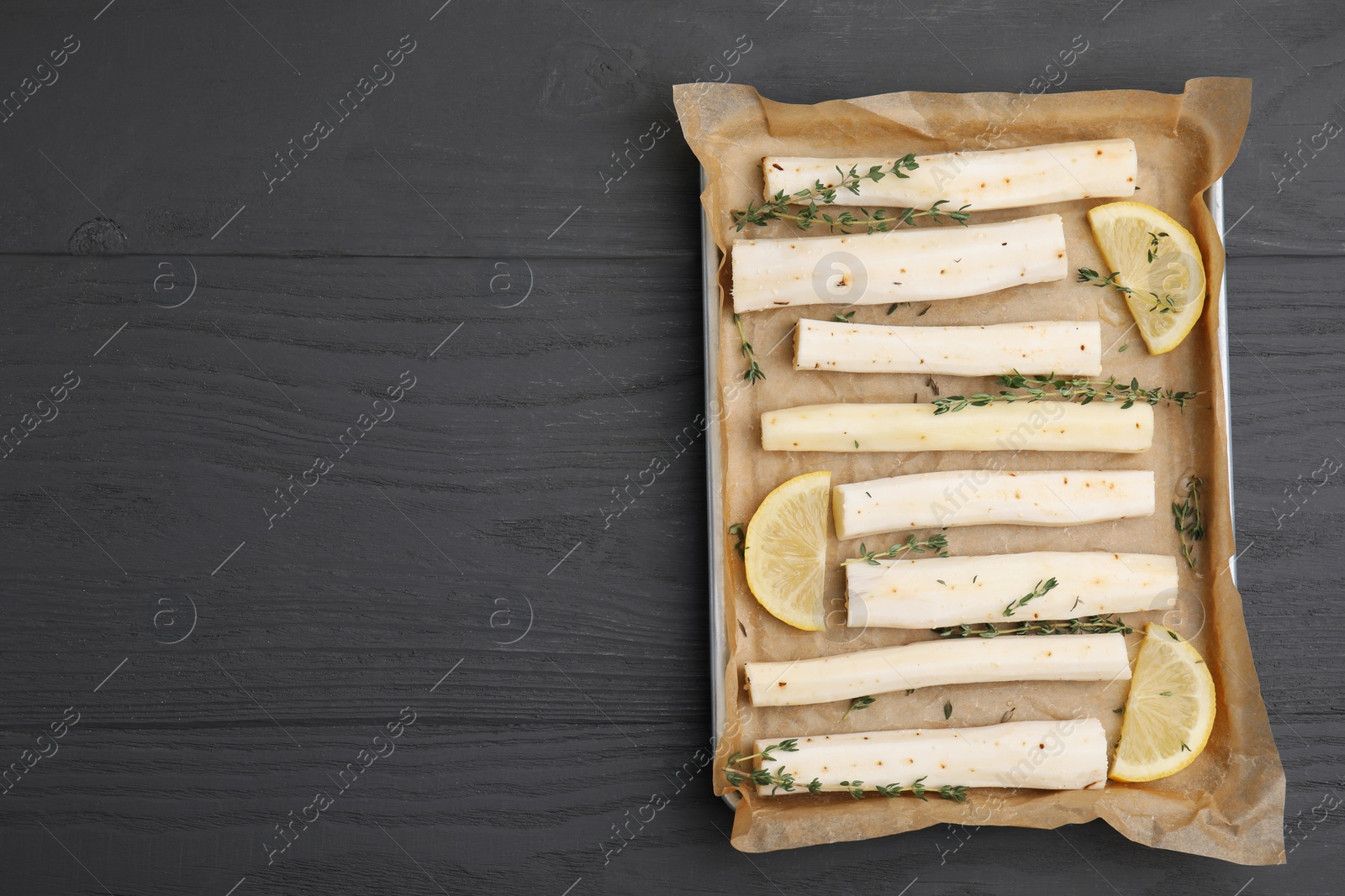 Photo of Baking tray with raw salsify roots, lemon and thyme on grey wooden table, top view. Space for text