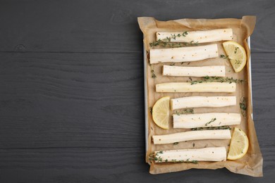 Baking tray with raw salsify roots, lemon and thyme on grey wooden table, top view. Space for text